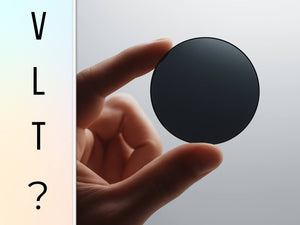 A hand holding a dark sunglass lens with the letters VLT on the side, symbolizing low light transmission sunglasses