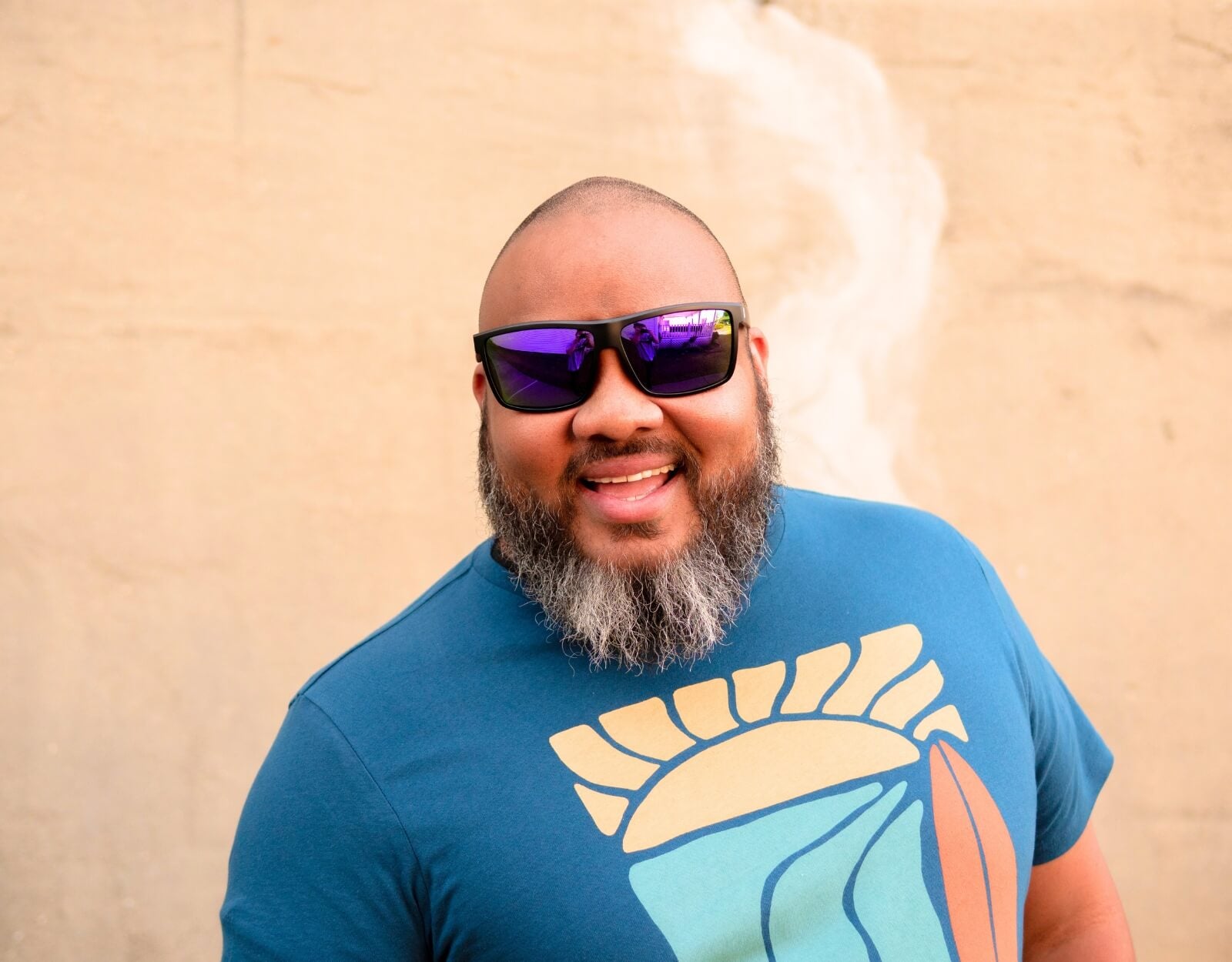 Bearded man wearing Faded Days sport sunglasses with mirrored lenses, smiling in a blue graphic shirt, representing athletic shades for big heads.