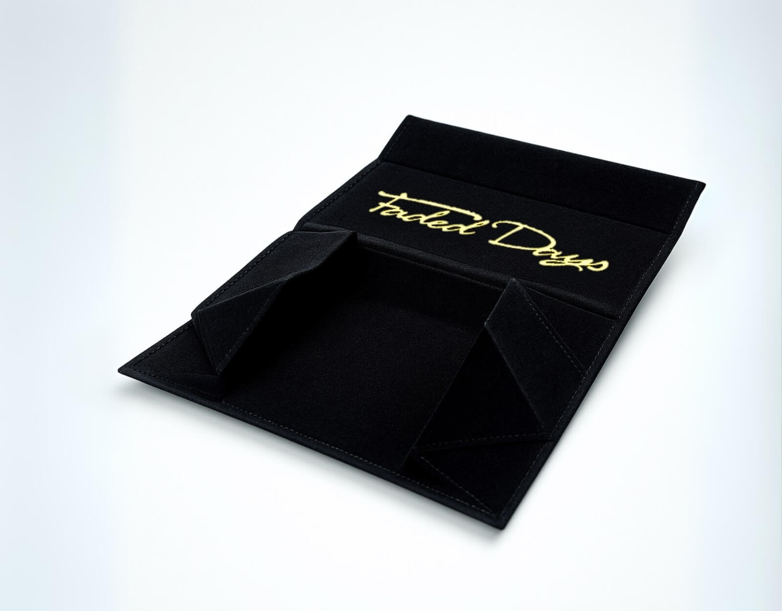Interior view of unfolded black collapsible sunglasses case with gold Faded Days logo on soft lining.