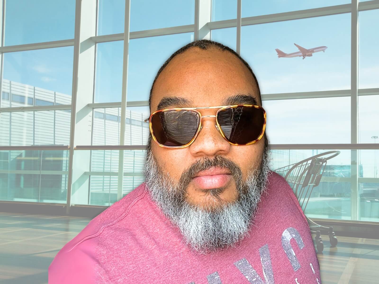 Man wearing sunglasses and a pink shirt in an airport setting